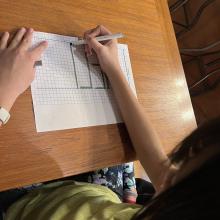 Child writes "Hello" backwards on a piece of paper in large block letters.