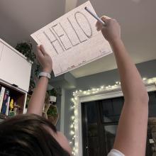 A child holds a piece of paper with "Hello" written on it up to the light.