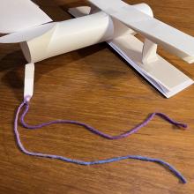 An airplane made out of construction paper with a string tied to the end.