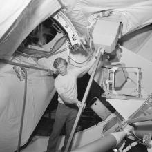 Black and white image of a man holding up a device in a space station simulator.