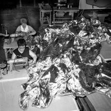 Black and white image of two women stitching together a parasol sunshade.