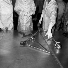 Black and white image of people in lab coats examining tools on a table.