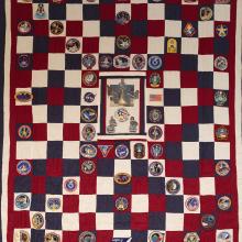 A quilt with red, white, and blue squares and mission patches.