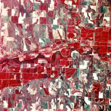 An aerial photo looking down at land, which looks red and green colored and split into irregular squares.