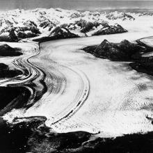 An aerial photograph of what looks to be a white river, but is actually a glacier cutting through the land.