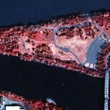 A near infrared aerial photo of a triangular shaped island that has a bridge connecting it to the mainland. The center of the island is a paler red.