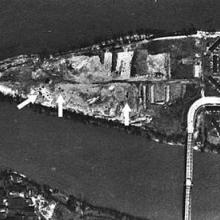 An aerial photo of a triangular shaped island that has a bridge connecting it to the mainland. Arrows point to dark patches on the southern parts of the island.