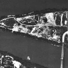 An aerial photo of a triangular shaped island that has a bridge connecting it to the mainland. AN arrow points to a channel in the middle of the island.