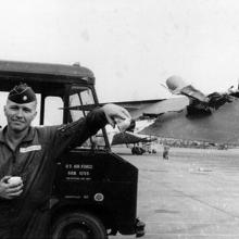 A uniformed man stands leaned up against a van that says U.S. Air Force on the side.