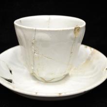 Small white teacup that has cracks in it and has been repaired