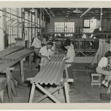 black and white photograph of men and women working on a large piece of corrugated metal