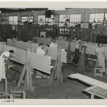 Black and white photo of men and women working on corrugated metal