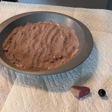 What appears to be dirt or cocoa flour in a pan. The pan sits on paper towels, there are rocks. 