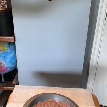 A hand is poised above a bowl of brown material. The hand holds a rock.