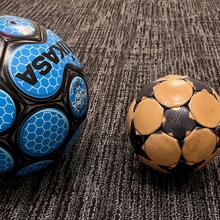 One large soccer ball and one smaller soccer ball sit side by side. 