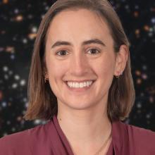 Portrait of a woman. She is smiling and wearing a burgundy shirt. Behind her is a star field.