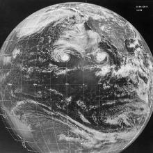 A black and white image of the earth with two swirling storms seen on its surface.