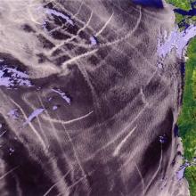 An image of the surface of part of the earth with wispy streaks of clouds over its surface.