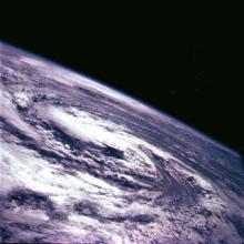 A circular swirl of clouds seen over the surface of the earth.