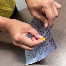 A photograph of a hand pushing a push pin through a maze print out. 