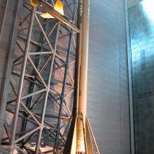 A large olive green rocket on display in a hangar with signage in front of it.