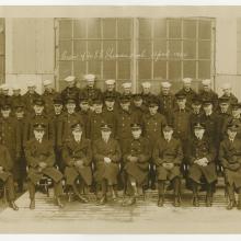  A partial view of a photograph of the entire crew of the USS Shenandoah in April 1924. A row of men sit posed in front of the camera with two rows of men standing behind them.