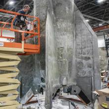 Large section of the bottom of a rocket is worked on inside a restoration facility.