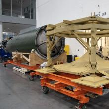 Center section of V2 rocket is attached to a launch table in a restoration facility.