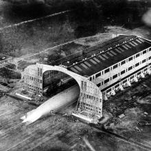 A view of the back half of Shenandoah from above as it is pulled out of its hangar. Hundreds of people can be see from the ground.