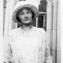 A woman with a hat stands in front of an architectural exterior. 