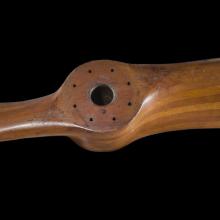 A wooden propeller is photographed against an all black backdrop.