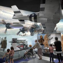 A rendering of a museum gallery with world war II aircraft hung from the ceiling and related objects on display.