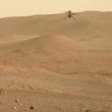 A small helicopter seen in the distance flying above the surface of Mars.