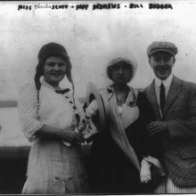 A woman on the left wears an an aviator's hat, she stands next two a woman and a man. 