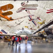 Planes both hand from the ceiling and stand on the ground in an aircraft hangar.