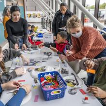 Young visitors sit at a table, decoration eclipse viewers, while assisted by adults. 