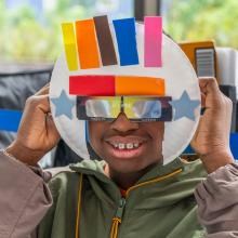 A young man shows off his eclipse viewing mask, created by adding a paper plate to eclipse glasses. 