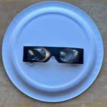 A pair of eclipse glasses sits on the back of a paper plate.