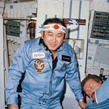 Ellison Onizuka onboard a spacecraft in space while wearing a flight suit and a bandana.