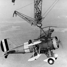 A small monoplane hangs from a hook high in the sky.