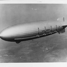 Large airship flies over land.