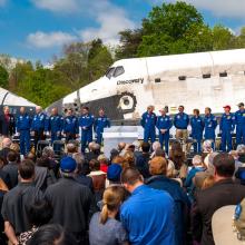 A group of astronauts stand next to two space shuttles that are nose to nose.