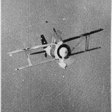 Biplane flies over water. The photo is taken from right in from of it while it is banked upwards. 