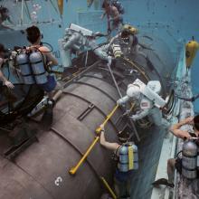 Astronauts participate in underwater training at NASA's Neutral Buoyancy Lab, practicing skills on a life-sized replica of a spacecraft module. Divers, wearing scuba gear, assist and observe the simulation.