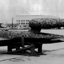 Vintage black and white image of a missile as it lays horizontally at an airfield.