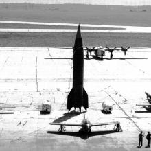 A missile stands in the middle of an airfield in a high contrast black and white image.