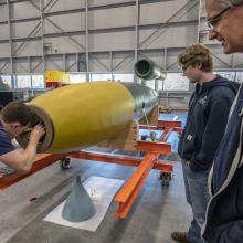 Three men inspect a missile in a restoration hangar.