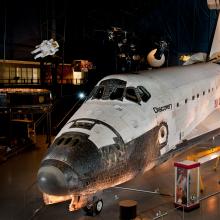 In a hangar dedicated to space artifacts at the Steven F. Udvar-Hazy Center, a space shuttle sits front and center. Space Shuttle Discovery looks like an oversized plane and its white paneling shows the wear and tear of flying in space. 