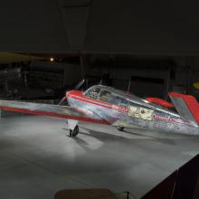 Silver and red painted single engine aircraft with V-tail. 