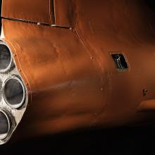 Side view of engine of an aircraft with three exhaust valves. The aircraft is painted orange. 